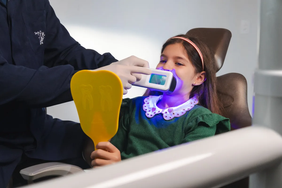 Odontopediatra usando QScan Plus com luz QLF azul em consulta com criança